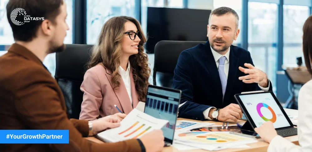 Business professionals in a meeting discussing growth strategies with charts, graphs, and laptops – Global Datasys Group, Your Growth Partner.